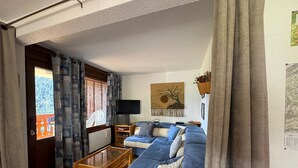 A living room with a blue sofa, a wooden coffee table, and a TV. - Charming 3-Room Apartment in Châtel - Pets Allowed & Parking (Châtel)