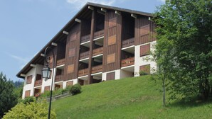 A multi-story building with wooden balconies and a sloped roof, surrounded by greenery. - Charming 3-Room Apartment in Châtel - Pets Allowed & Parking (Châtel)