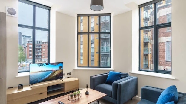 A modern living room with a large TV, two sofas, a coffee table, and large windows offering city views. - Bright 2 Bedroom Apartment in Central Manchester (Manchester)