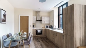 A modern kitchen with wooden cabinets, a glass dining table, and a window with a view. - Bright 2 Bedroom Apartment in Central Manchester (Manchester)