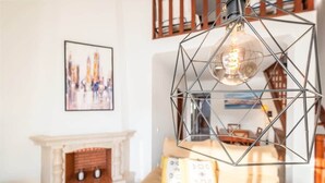Un salon moderne agrémenté d’un luminaire suspendu aux formes géométriques, d’une cheminée et d’un tableau représentant un paysage urbain, encadré.