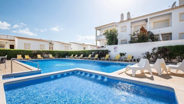 Une piscine avec des chaises longues, un ciel dégagé et un bâtiment doté de balcons.