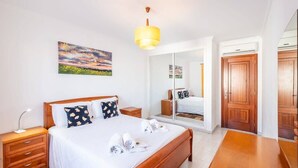 Une chambre d’hôtel avec un lit, des tables de chevet, un miroir, une porte en bois et un tableau au mur.