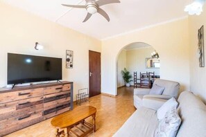 Un salon avec un téléviseur à écran plat posé sur un meuble en bois, un ventilateur de plafond, un canapé et une table à manger.