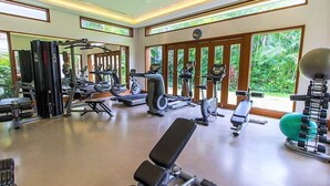 Un gimnasio con diverso equipamiento de ejercicio, amplias ventanas y vistas a zonas verdes.