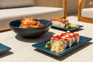 A table with three dishes: a bowl of salad, a plate of sushi, and a plate of sushi with toppings.