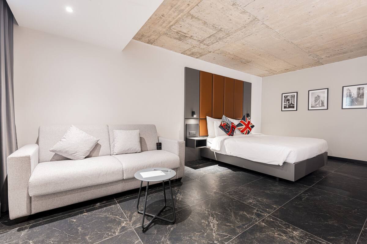 Una habitació d'hotel moderna amb un sofà, un llit, una taula petita i obres d'art a les parets.
