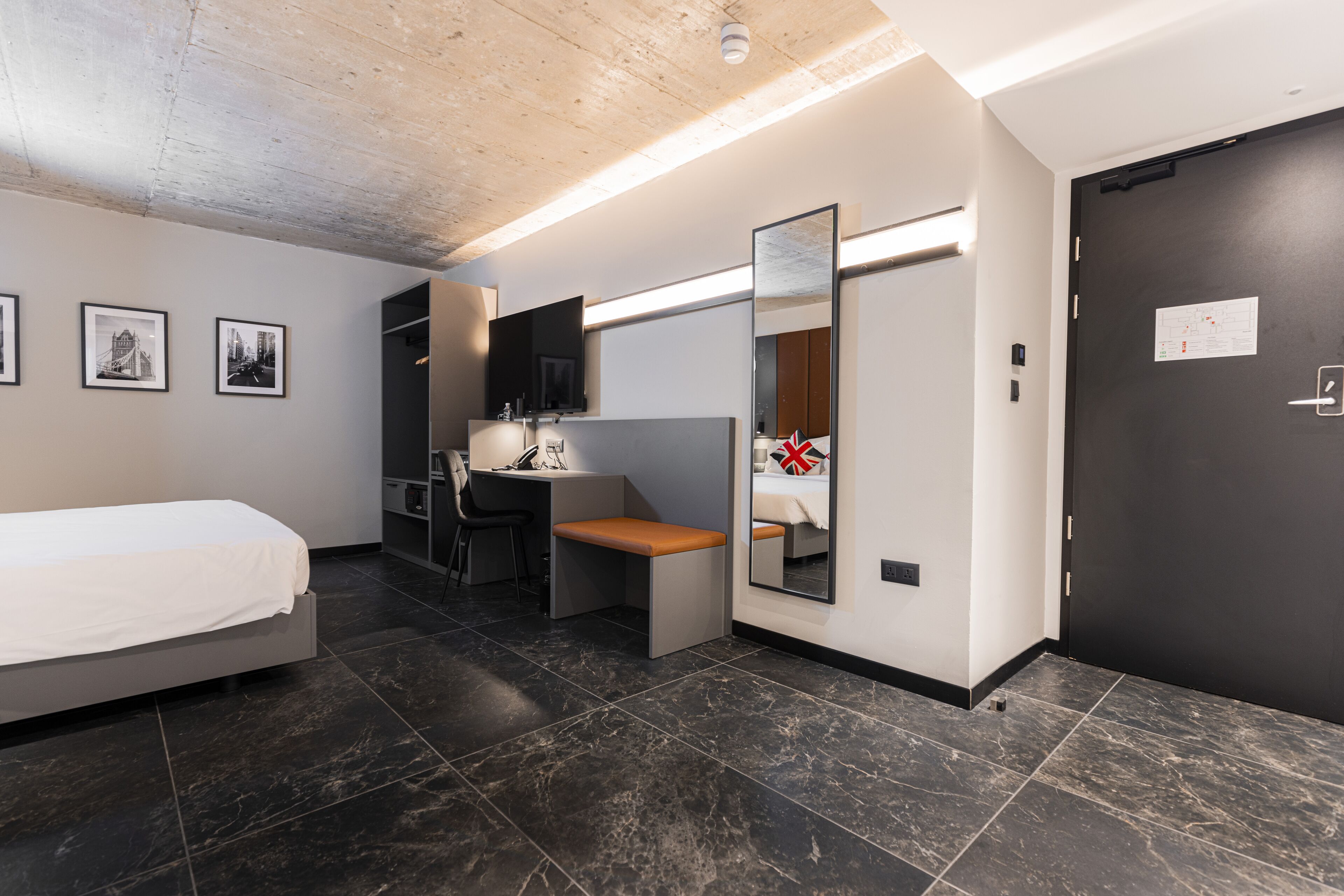 A modern hotel room with a bed, desk, chair, and a large mirror.