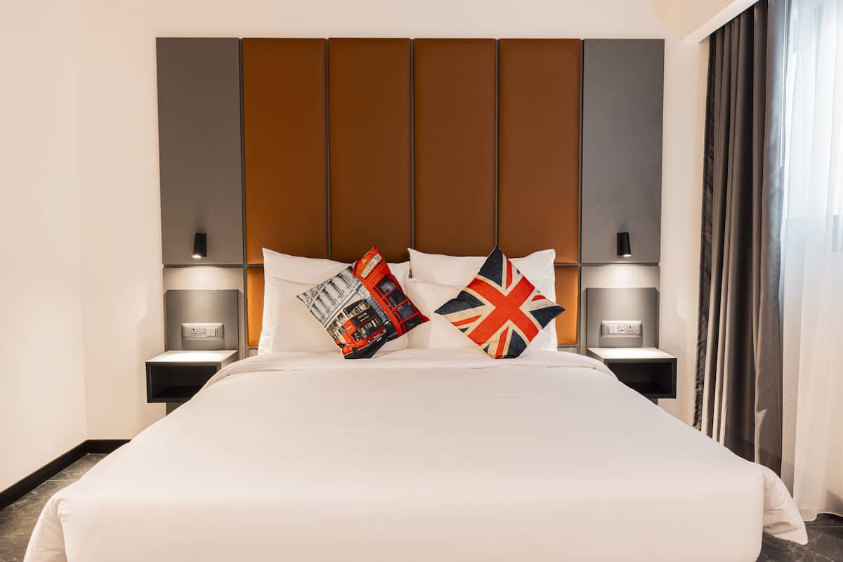 Una habitació d'hotel amb un llit gran, dues taules de nit amb làmpades, un capçal modern i vista a una ciutat a través de la finestra.