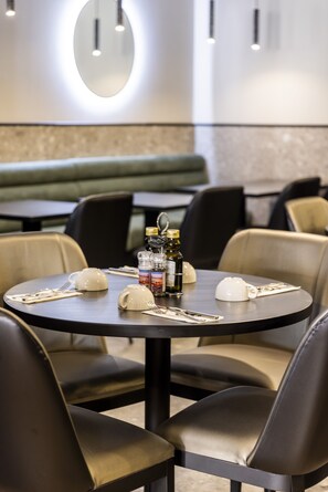 A restaurant with round tables, black chairs, and a green booth. - The Londoner Hotel St. Julians (St. Julian's)