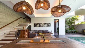 A modern living room with a wooden table, wicker pendant lights, a sofa, and a staircase. - Best Seller 2 Bedrooms Villa in Central Seminyak (Seminyak)