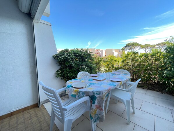A patio with a table set for four, surrounded by white chairs, under a clear sky.