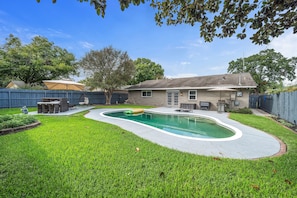 A backyard with a swimming pool, a barbecue area, and a house.