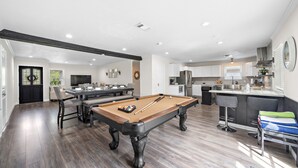 Un grand espace de vie comprenant un billard, une table à manger et un coin cuisine.