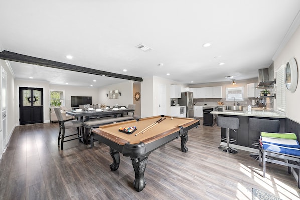 A spacious living area with a pool table, a dining table, and a kitchen area.