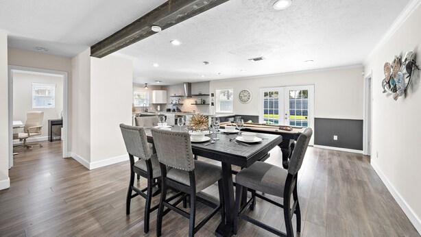 Un vaste espace à manger avec une table en bois foncé et des chaises assorties, une cuisine en arrière-plan et une vue sur l’extérieur grâce à de grandes fenêtres.