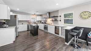 Une cuisine moderne avec des meubles blancs, un îlot central et un coin bar avec des tabourets.