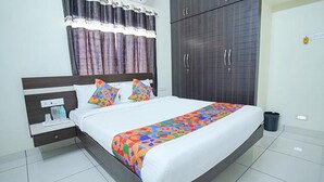 A neatly made bed with a colorful bedspread, a bedside table with a water bottle, and a wardrobe with two doors. - Fabexpress Srinivasan Apartment (Vandavasi)