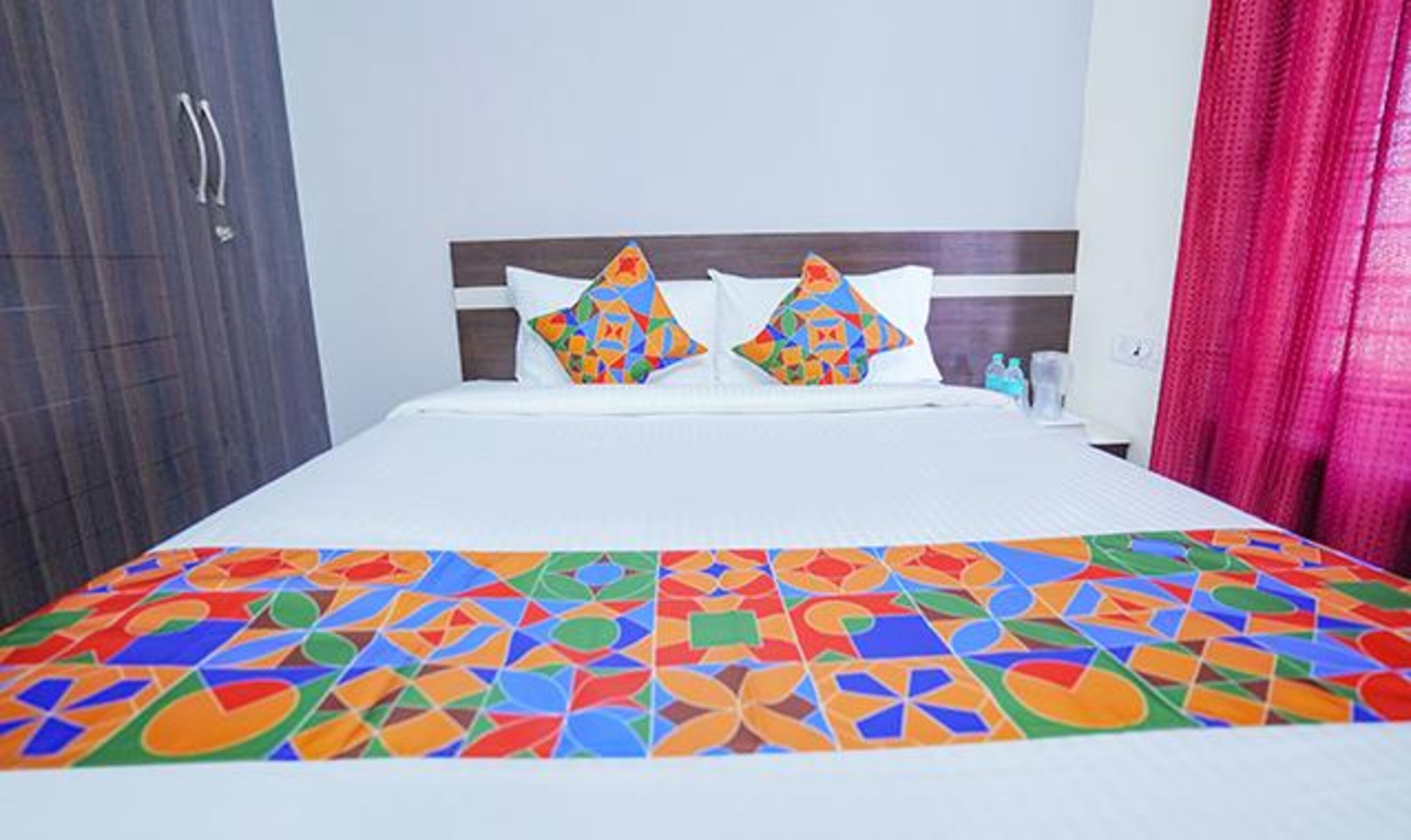 A hotel room with a bed, pillows, and a colorful bedspread.