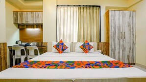 A hotel room with a bed, two pillows, a desk with a chair, a window with curtains, and a wardrobe. - Fabhotel Happy Stay (Pune)