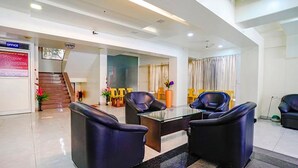 A modern hotel lobby with a reception desk, a staircase, and several black leather chairs. - Fabhotel Happy Stay (Pune)