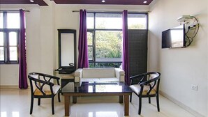 Una habitación con sofá, dos sillones, una mesa, televisor y ventana con cortinas.