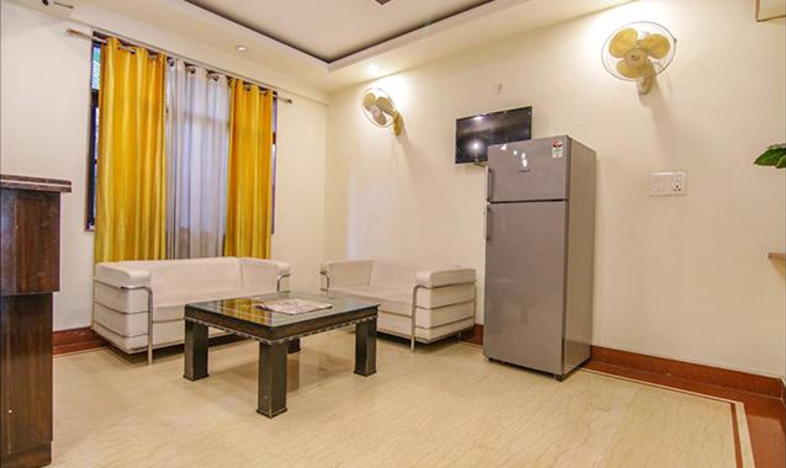 Una sala de estar con sofá, una mesa de centro, un refrigerador y un televisor instalado en la pared.