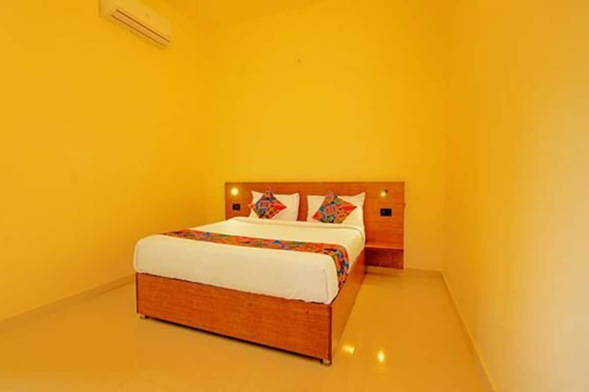 A single bed with a wooden headboard, white bedding, and colorful pillows in a room with yellow walls and a light-colored floor.