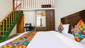 A bedroom with a bed, colorful pillows, a wooden headboard, a desk with a chair, and a staircase. - Fabhotel Wildflower Inn (Nainital)