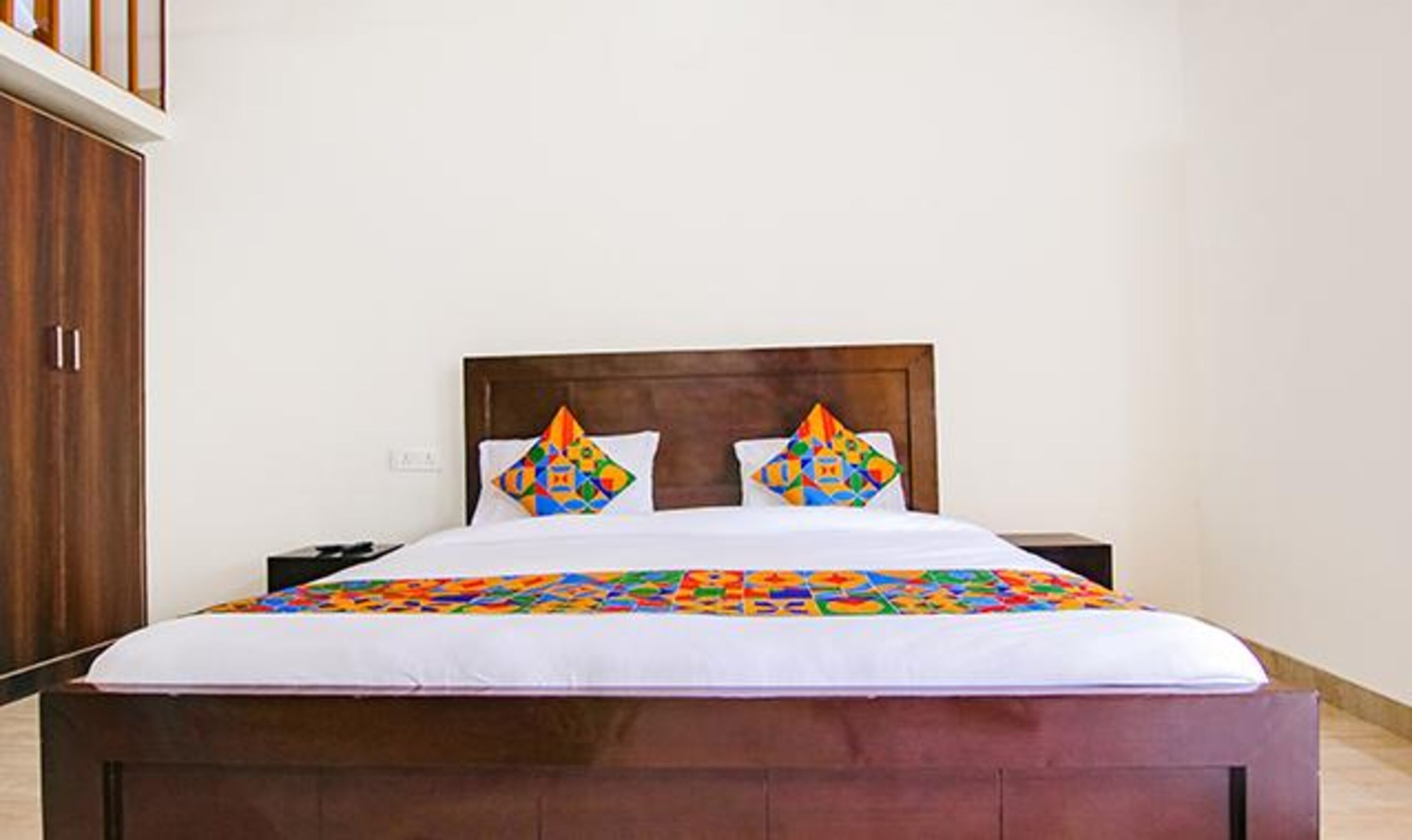 Una habitación de hotel estándar con un cabecero de madera, ropa de cama blanca y almohadas de colores con diseños geométricos.