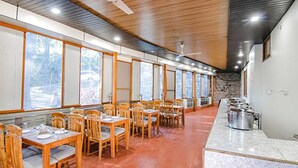 A restaurant with wooden tables and chairs, large windows, and a stone wall. - Fabhotel Wildflower Inn (Nainital)