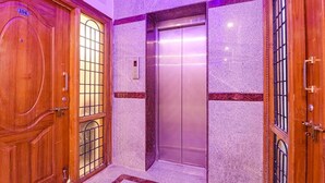 A wooden door with a glass panel and a number plate, an elevator, and a marble wall with a red border. - Fabhotel Elite Inn (Bengaluru)