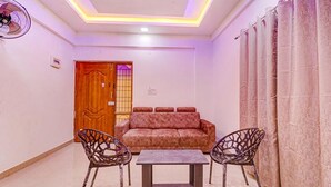 A living room with a sofa, two chairs, a small table, a ceiling fan, and a door. - Fabhotel Elite Inn (Bengaluru)