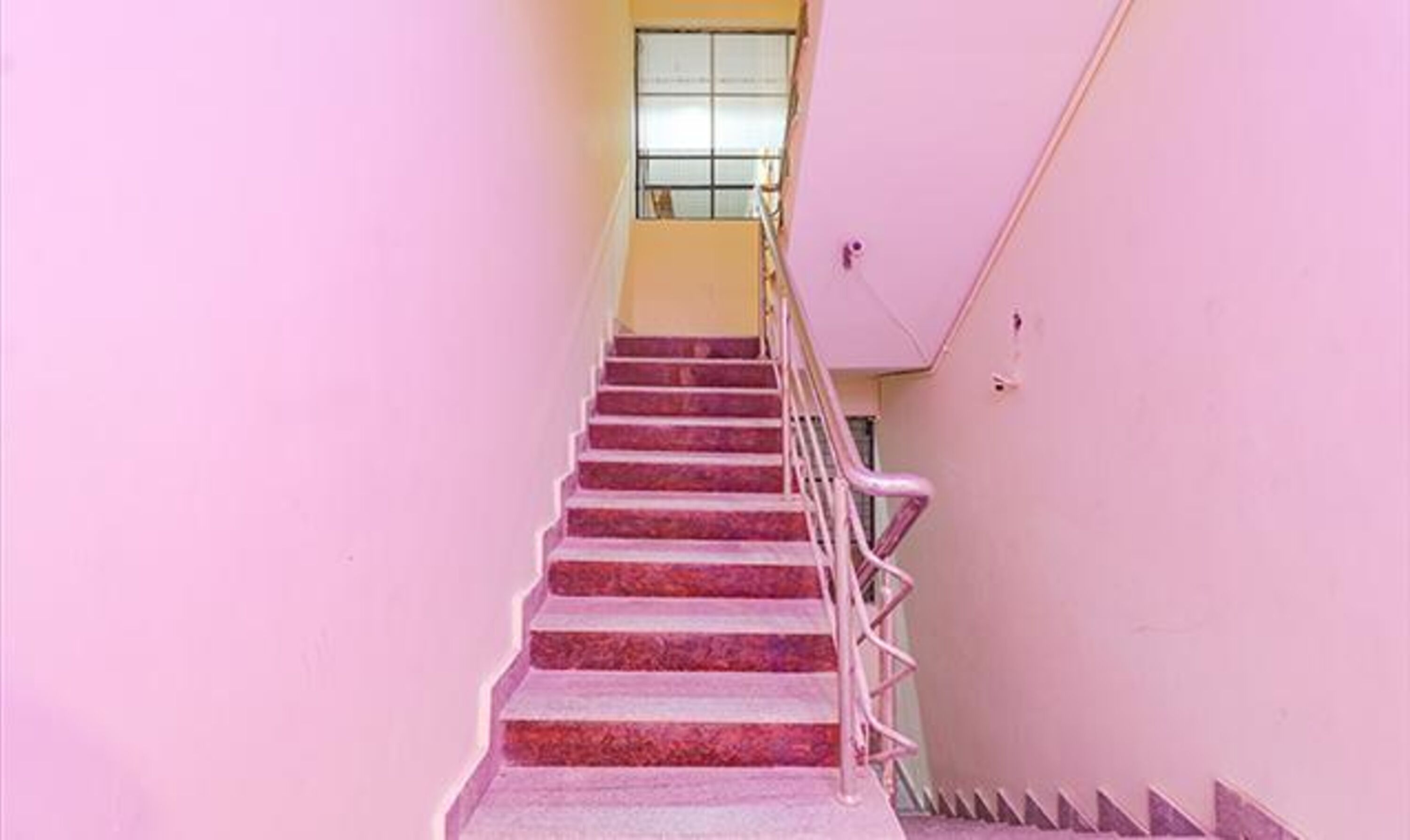 Una escalera con paredes rosas y barandilla de metal.