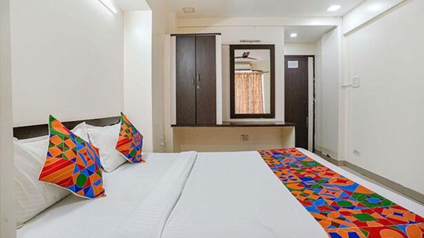 A hotel room with a bed, two pillows, a window, a mirror, and a door. - Fabexpress Jasmin Rooms (Pune)