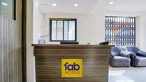 A reception desk with a 'fab hotels' sign, a window with blinds, and a seating area with two sofas. - Fabexpress Jasmin Rooms (Pune)