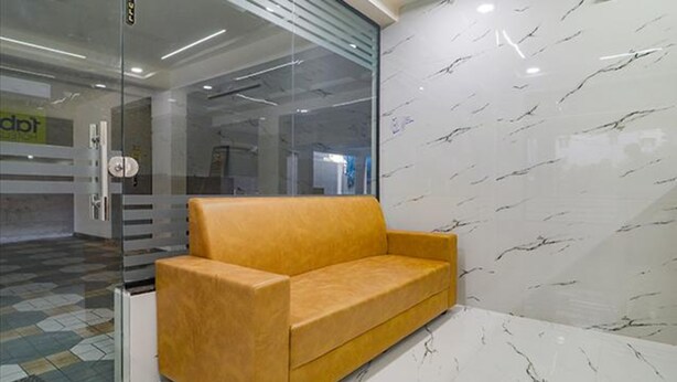 A modern office space with a glass partition, a yellow sofa, and a marble-patterned wall. - Fabhotel Stone Gallery (Hyderabad)