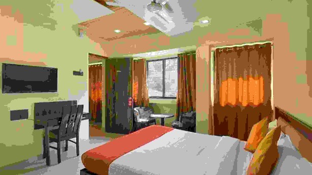 Una habitació d'hotel amb un llit, escriptori, cadira i finestra amb cortines.