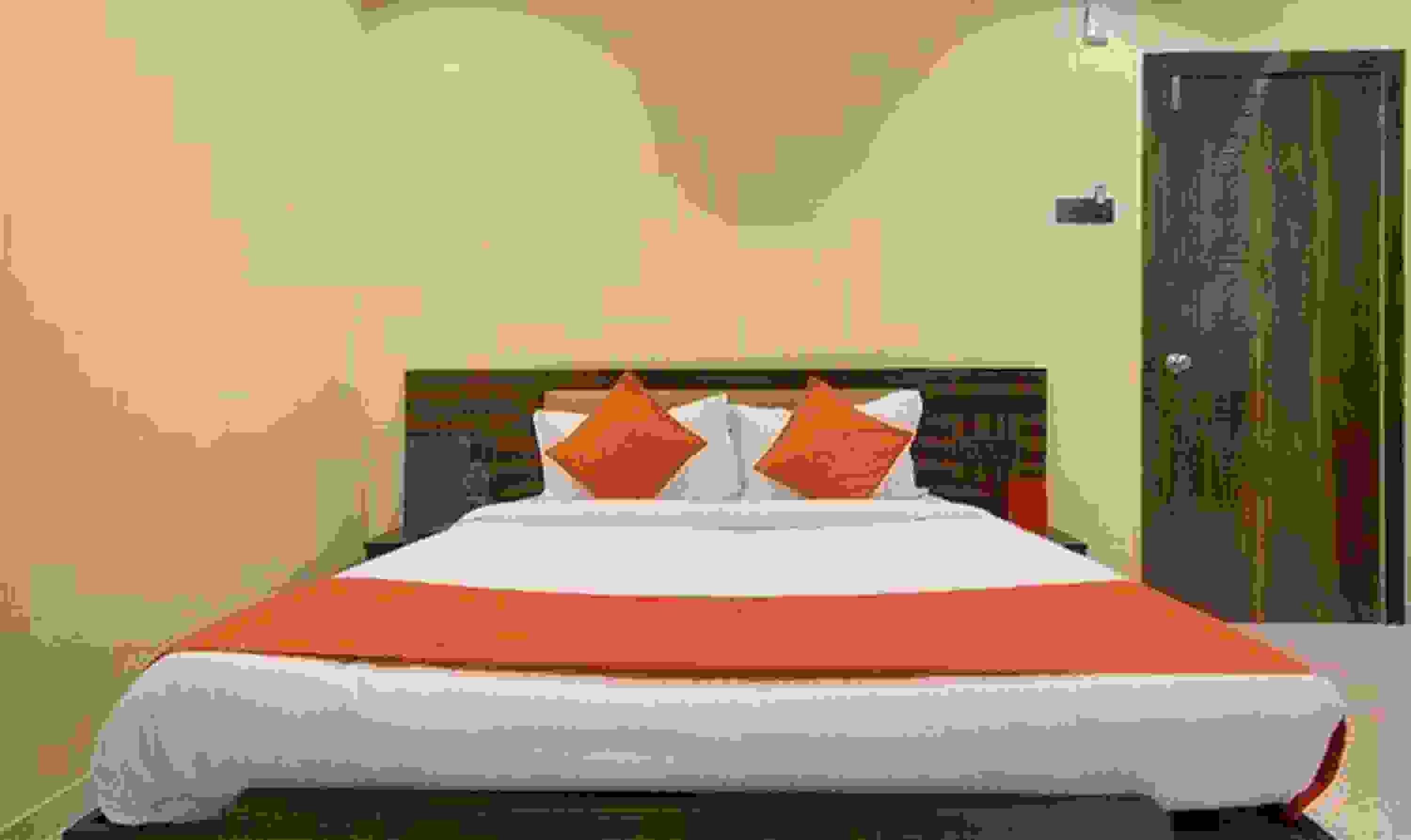 A bed with a red and white bedspread, two orange pillows, and a headboard with a patterned design.