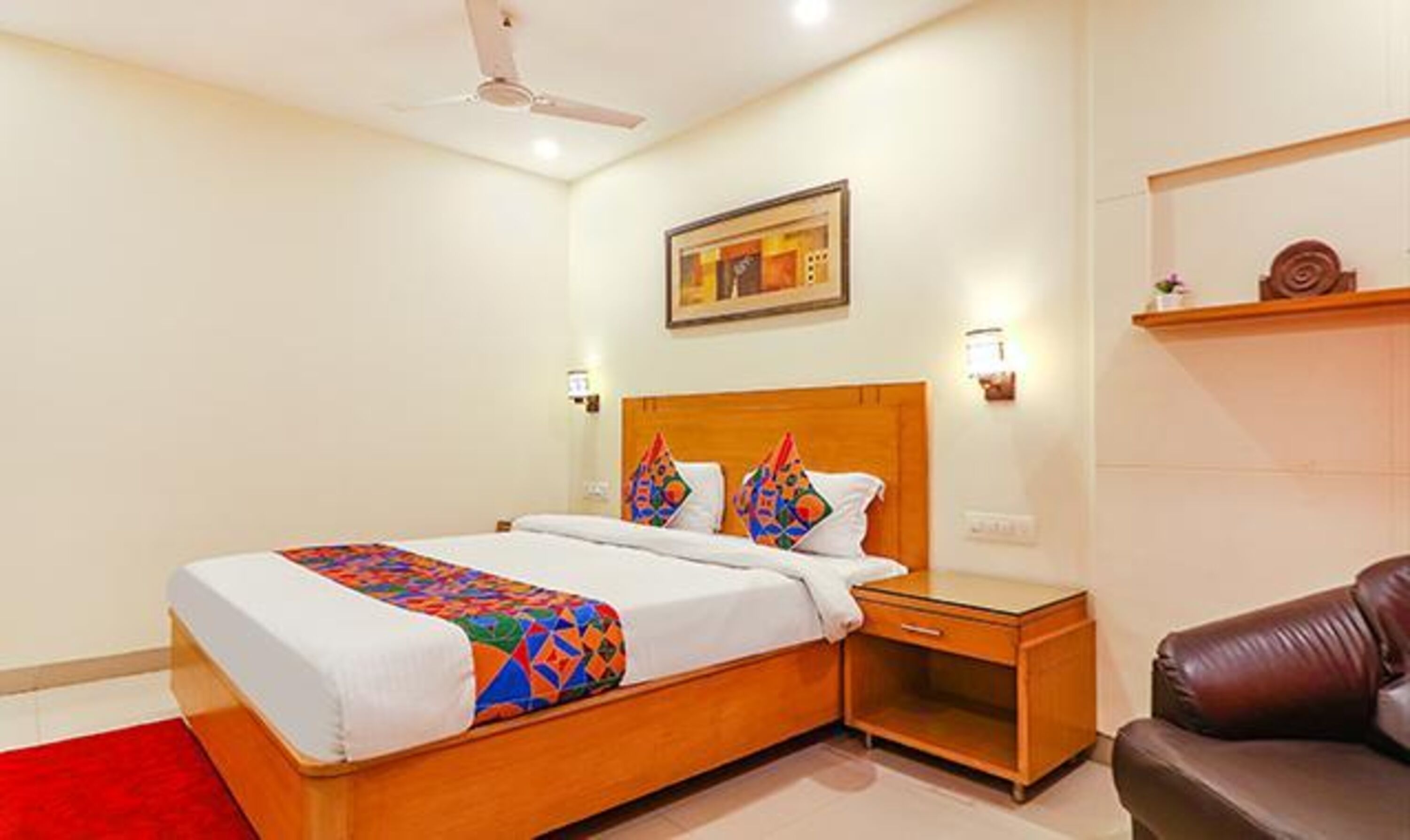 A hotel room with a wooden bed, a red carpet, a nightstand, a brown leather chair, and a painting on the wall.