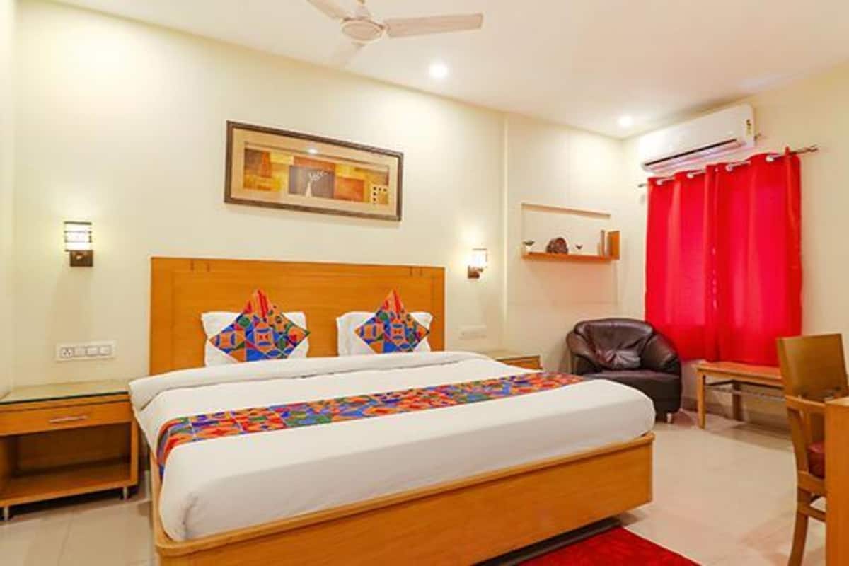 A hotel room with a bed, a desk, a chair, a ceiling fan, and a red curtain.