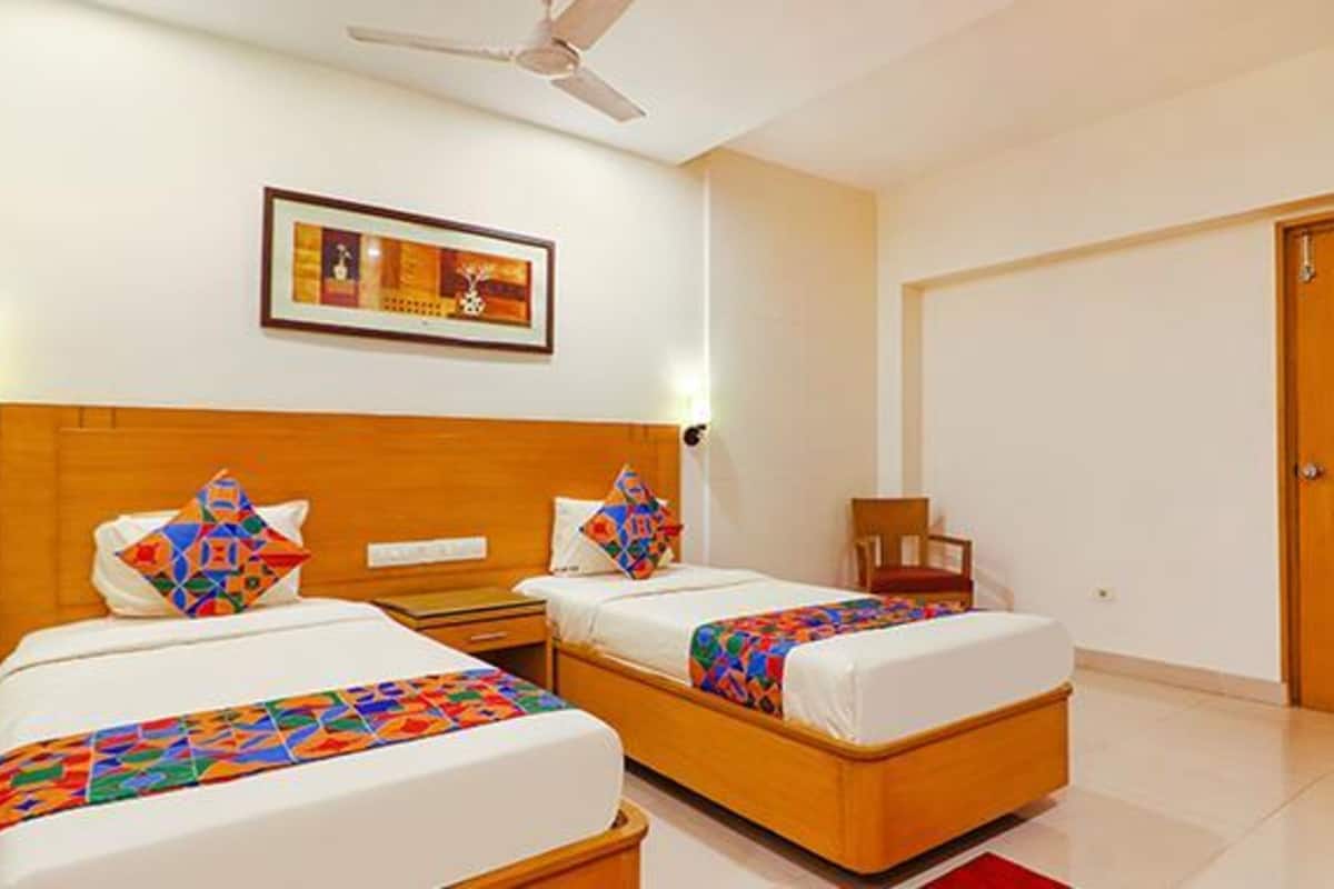 A hotel room with two beds, a ceiling fan, a framed picture on the wall, and a wooden door.