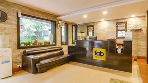 Ein Empfangsbereich mit Steinwand, einer Rezeption, einer Couch und einem Fenster mit Blick auf Grünflächen.