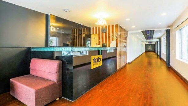 Et hotelreception område med et moderne design, inklusive en receptionsdisk, et siddeområde med en lyserød stol, og et skilt med hotellets navn.