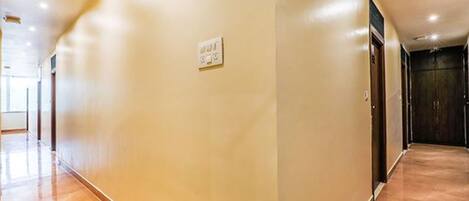 A corridor with a light-colored wall, a power outlet, and a wooden floor.