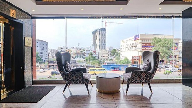 A hotel lobby with two patterned armchairs and a round coffee table, a large window offering a city view with buildings and a construction crane. - Fabhotel Twin Tree Suites (Hyderabad)