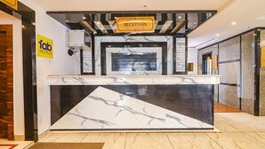 A hotel reception area with a marble counter, a reception desk, and a sign indicating the reception. - Fabhotel Twin Tree Suites (Hyderabad)