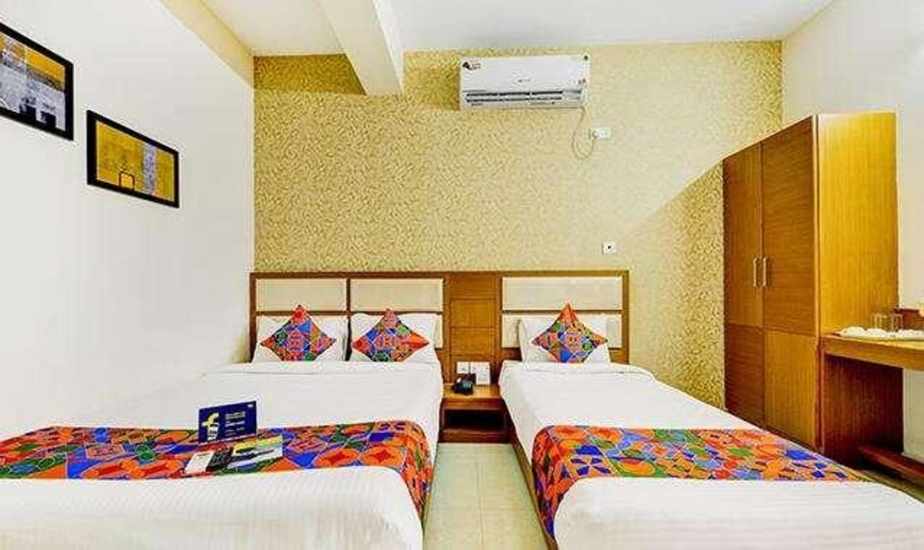 A hotel room with two beds, a wooden wardrobe, and an air conditioning unit on the wall.