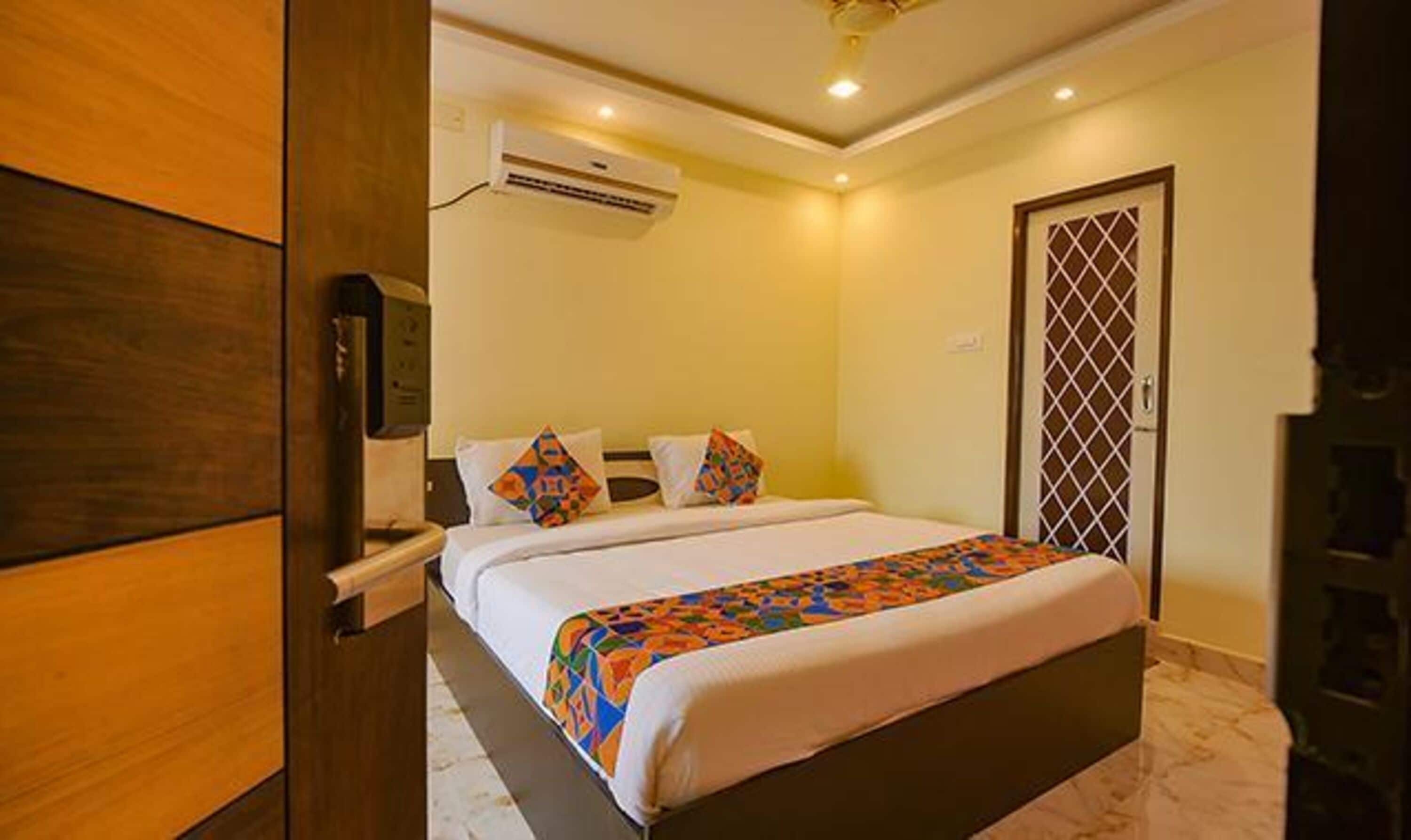 A hotel room with a bed, a wooden wardrobe, an air conditioning unit, and a door with a lattice design.