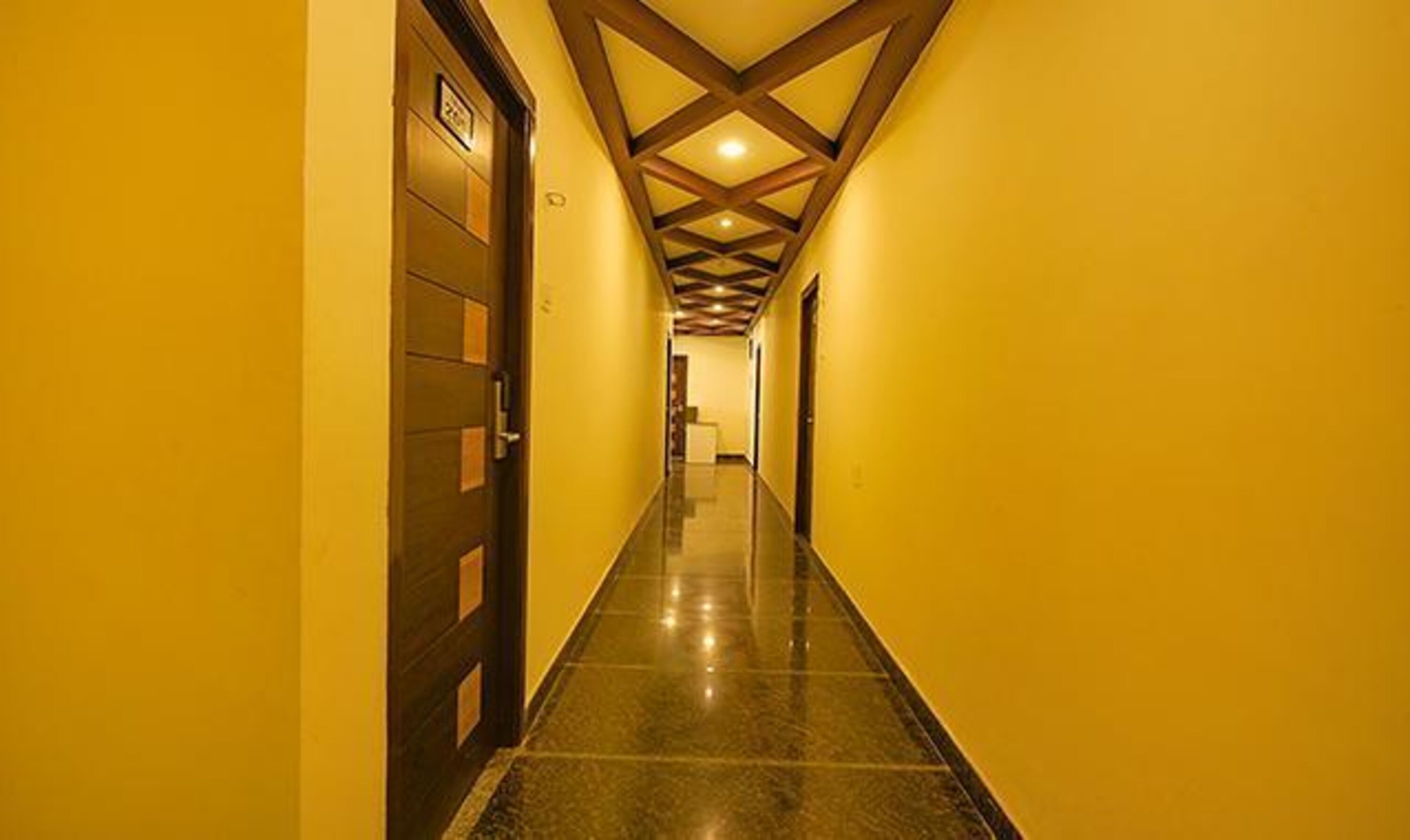 A hallway with yellow walls, a polished black floor, and wooden ceiling beams.